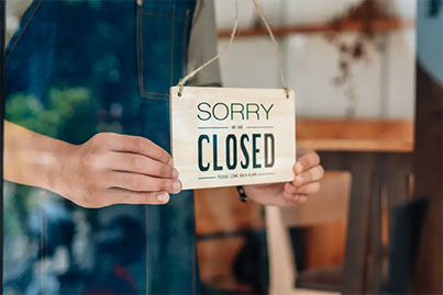 Shop owner hanging a 'Sorry We're Closed' sign, representing closing or dissolving a business